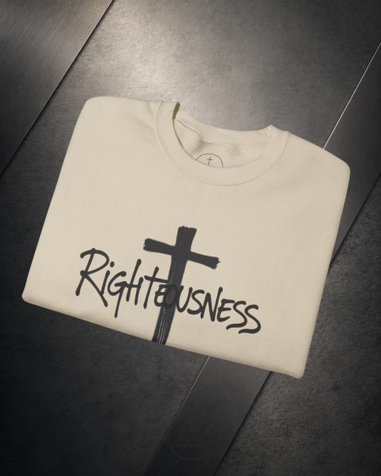 Folded beige sweatshirt with a black cross and 'Righteousness' text on a dark surface