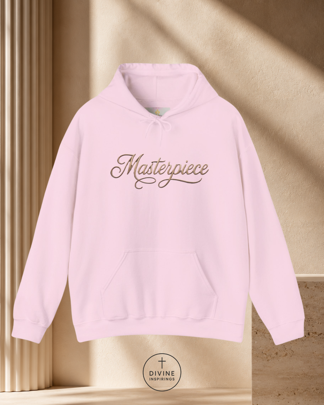 Pink hoodie with 'Masterpiece' text on a beige background