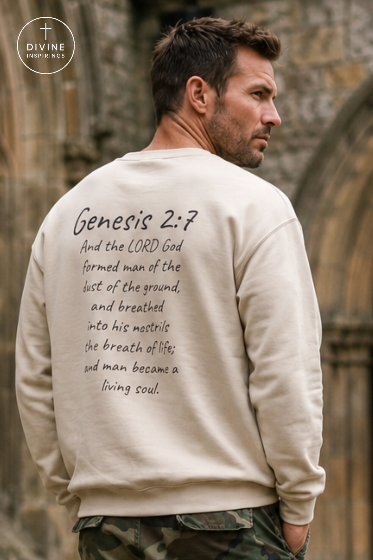A man wearing a cream-colored sweatshirt with a Bible verse printed on the back, shown from behind in an outdoor setting with a stone wall background.