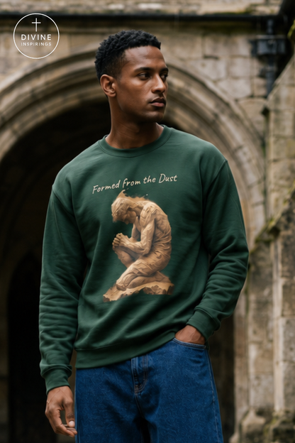 A man wearing a dark green crewneck sweatshirt with a graphic of a kneeling figure and the text 'Formed from the Dust', paired with blue jeans, standing in front of a stone archway. A 'Divine Inspirings' logo is visible in the top left corner.