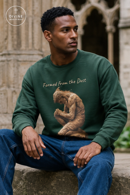 A man wearing a dark green crewneck sweatshirt with a graphic of a seated figure and the text 'Formed from the Dust' on the front, paired with blue jeans, sitting outdoors against a stone wall.