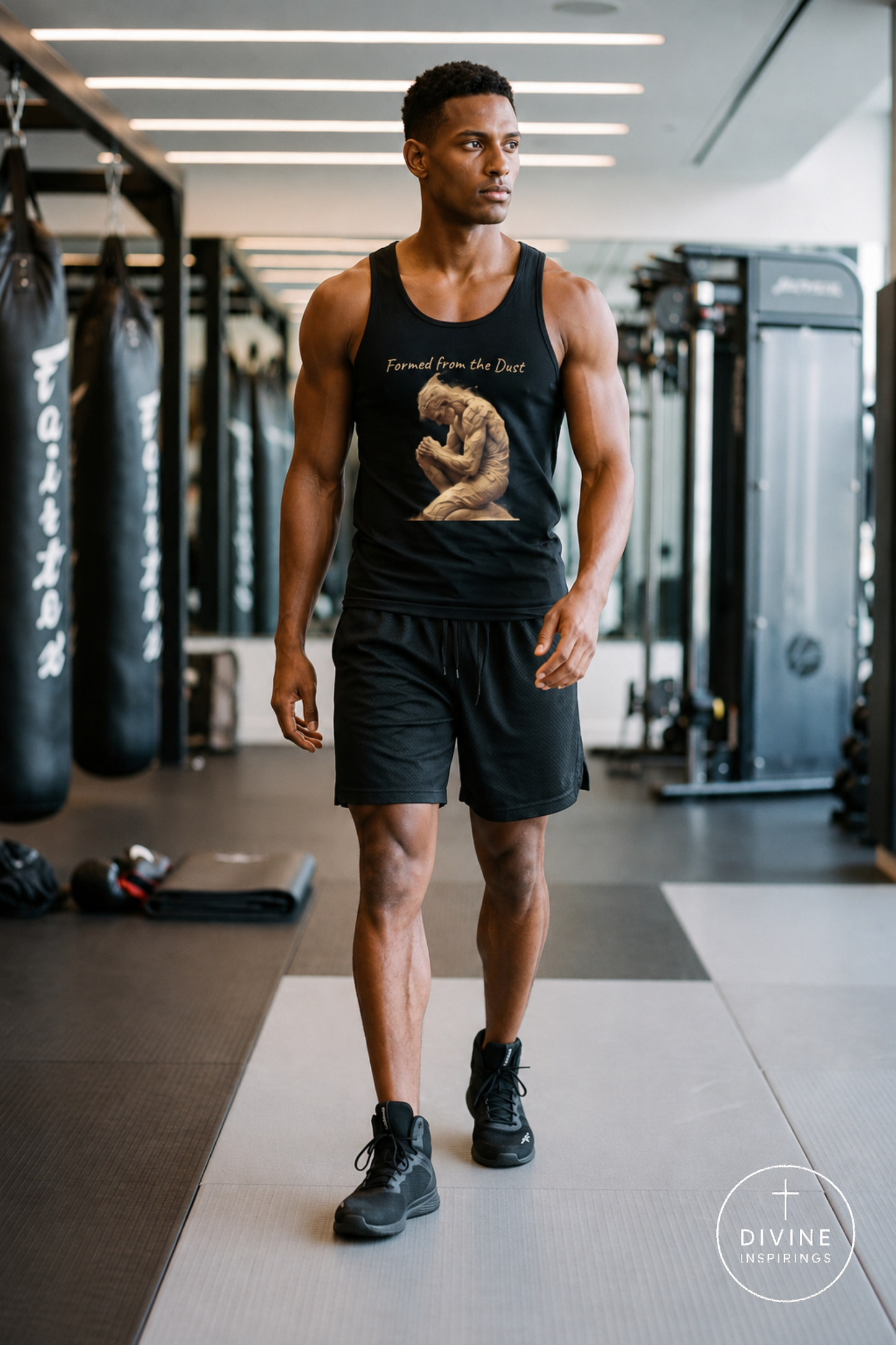 A man walking in a gym wearing a black tank top with a graphic print that reads 'Formed from the Dust' and a beige figure, paired with black shorts and black sneakers. The background shows gym equipment and punching bags.