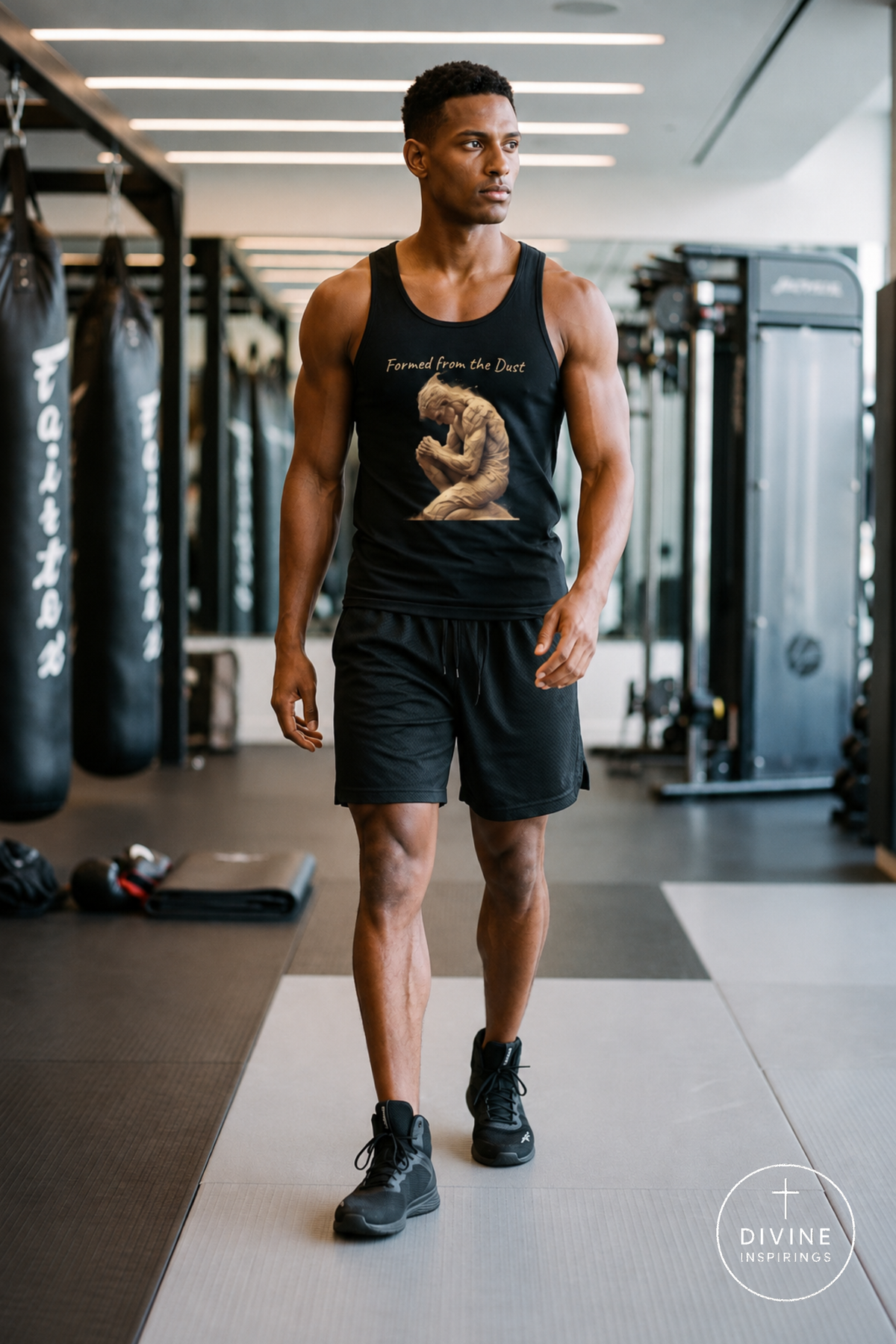 A man walking in a gym wearing a black tank top with a graphic print that reads 'Formed from the Dust' and a beige figure, paired with black shorts and black sneakers. The background shows gym equipment and punching bags.