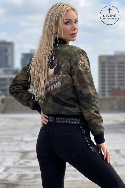 A blonde woman wearing a camouflage bomber jacket with a large graphic print on the back, styled with black jeans and a studded belt, posing outdoors with a city skyline in the background. A 'Divine INSPIRINGS' logo is visible in the top right corner.