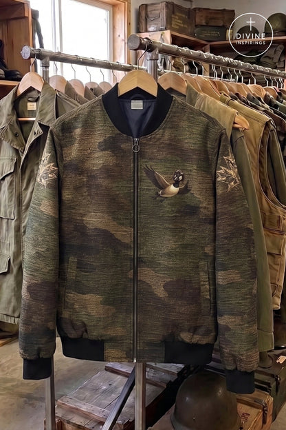 A camouflage bomber jacket with a goose graphic on the chest, displayed on a clothing rack inside a shop.