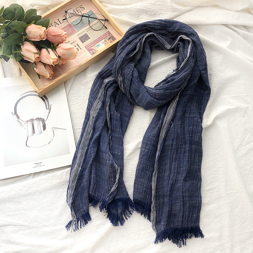 Blue scarf on a white surface with a book, glasses, and flowers in the background