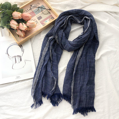 Blue scarf on a white surface with a book, glasses, and flowers in the background