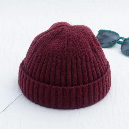 Maroon knit beanie on a white background with green sunglasses.