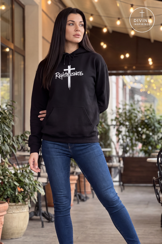A woman modeling a black pullover hoodie with a white cross and the word 'Righteousness' printed across the chest, paired with blue skinny jeans in an outdoor patio setting.
