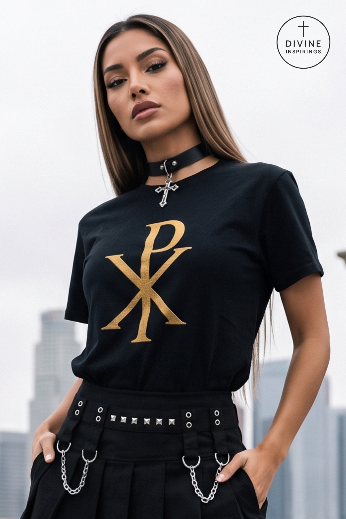 A woman wearing a black short-sleeve t-shirt with a large gold Chi-Rho monogram on the front, styled with a black choker necklace and black pants against an overcast sky background.