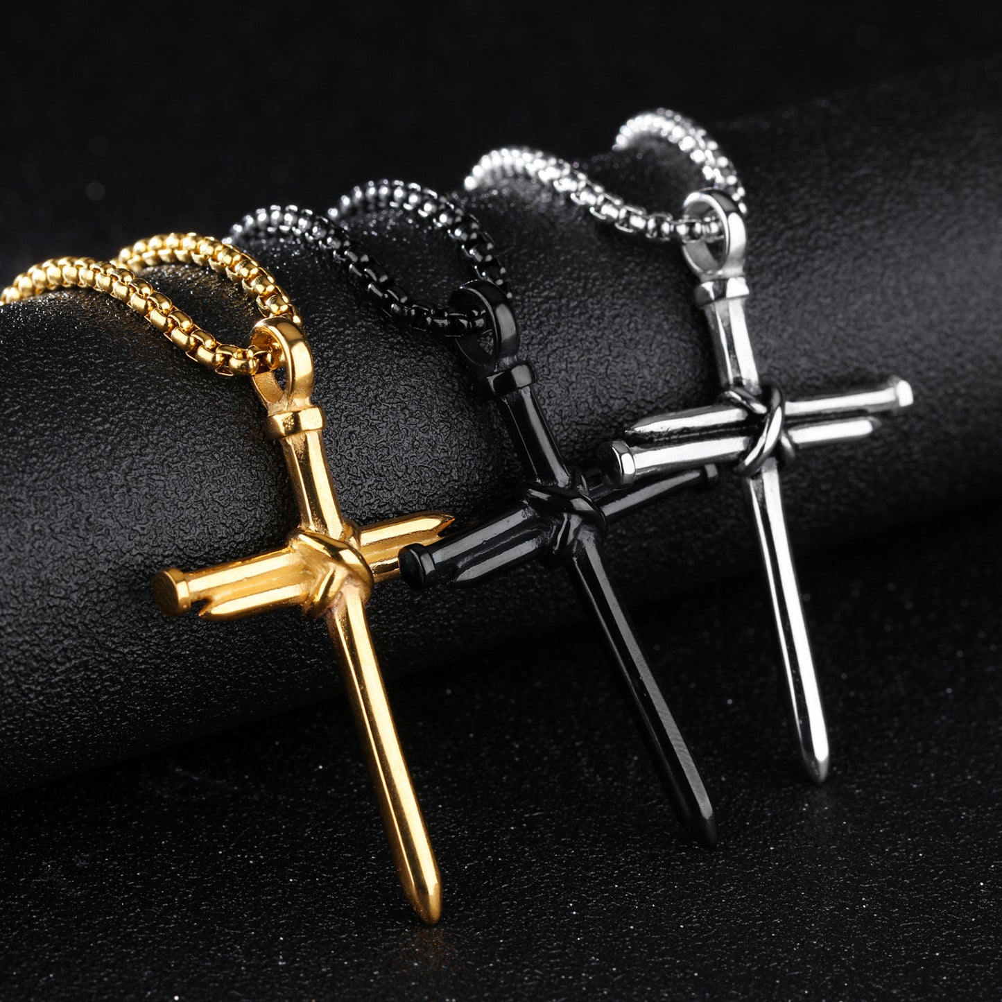 Three cross-shaped necklaces in gold, silver, and black on a dark background