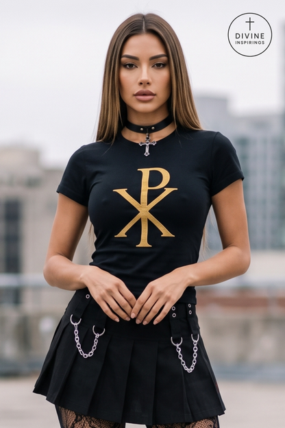 A woman wearing a black short-sleeve t-shirt with a large gold Chi-Rho monogram on the front, paired with a black pleated mini skirt featuring silver chain details. She is wearing a black choker with a cross pendant.
