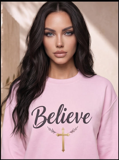 Woman wearing a pink sweatshirt with 'Believe' and a cross design.
