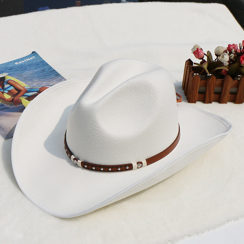 White cowboy hat with a brown band on a white surface with a magazine and decorative items.