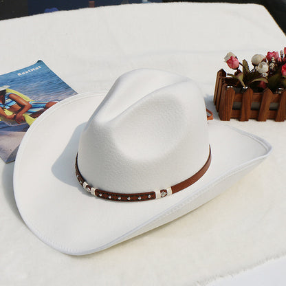 White cowboy hat with a brown band on a white surface with a magazine and decorative items.