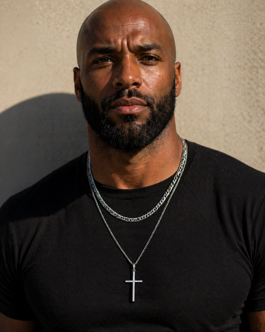 Man wearing a black t-shirt and a necklace with a cross pendant against a neutral background