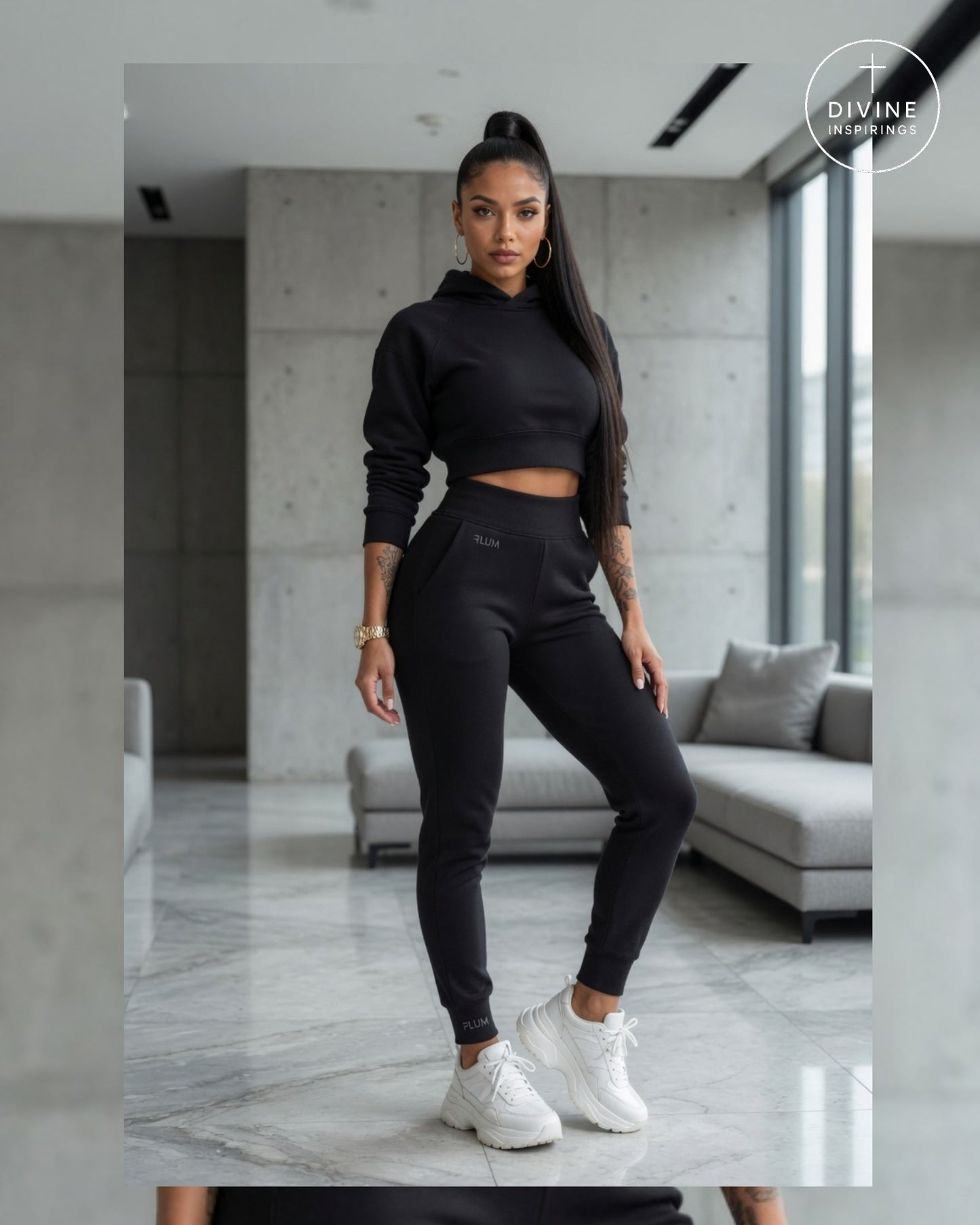 A woman modeling a black two-piece activewear set consisting of a cropped long-sleeve hoodie and matching jogger pants, paired with white sneakers, in a modern living room setting.