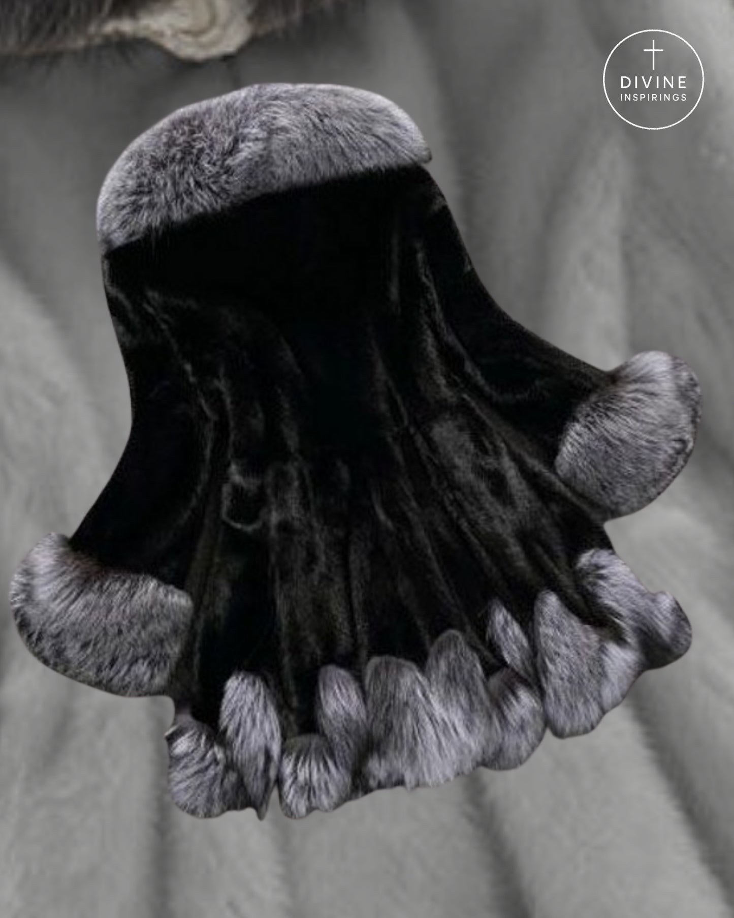 A black velvet hood or cape with plush gray fur trim at the top, sides, and bottom hem, displayed against a soft gray fabric background. A circular 'DIVINE INSPIRINGS' logo is visible in the upper right corner.