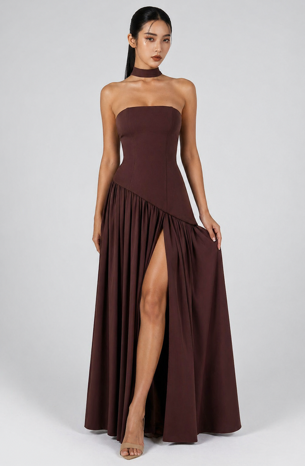 Woman wearing a strapless brown dress with a high slit on a white background