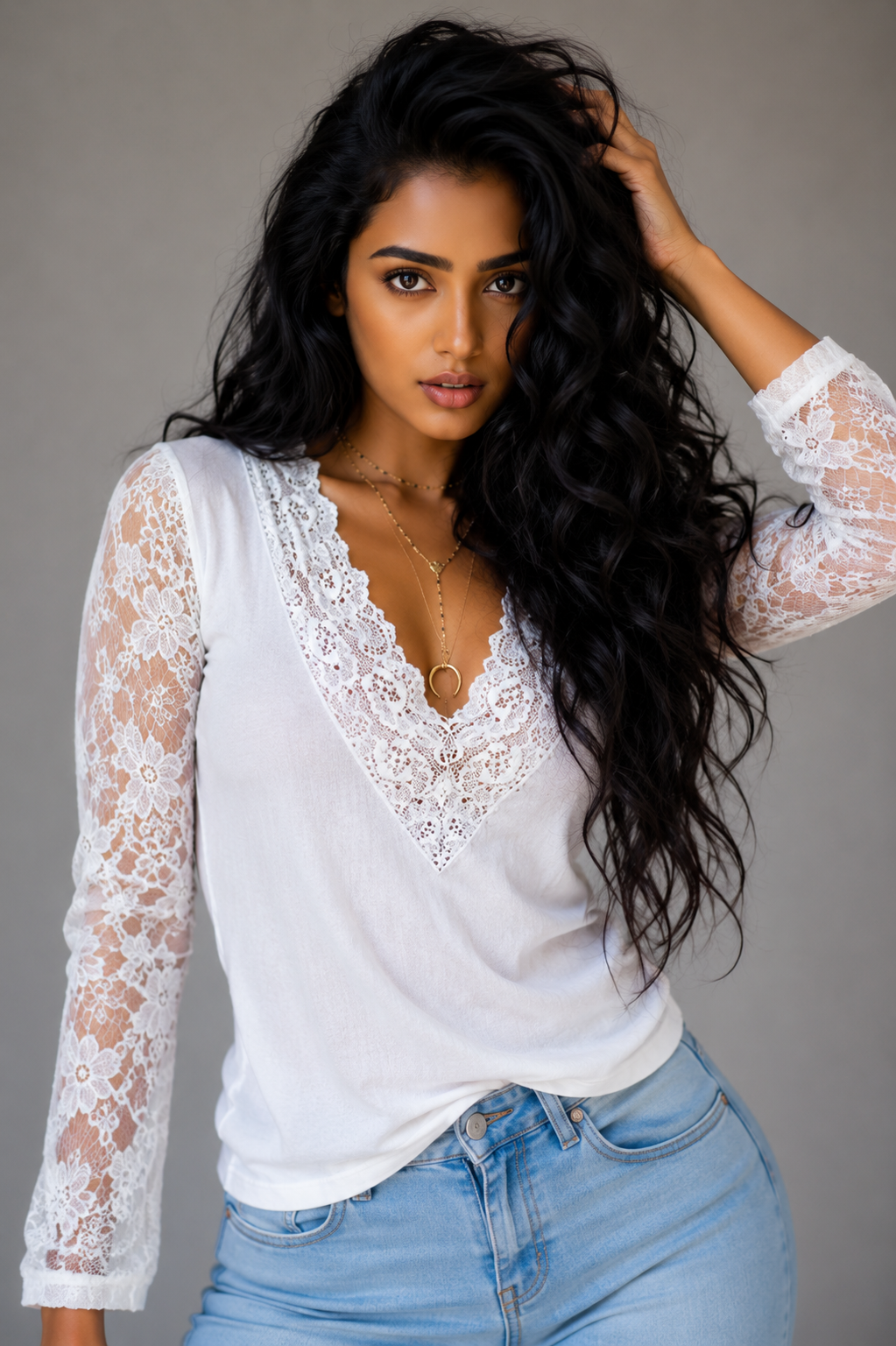 Woman wearing a white lace top and blue jeans against a gray background