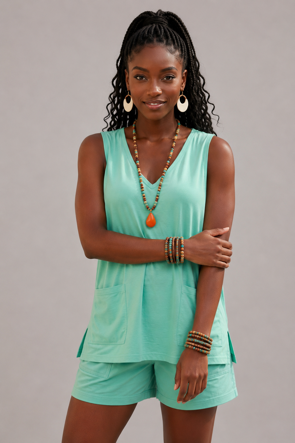 Woman wearing a mint green sleeveless top and shorts set with jewelry on a gray background