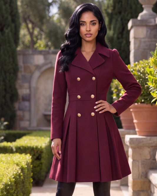 A woman wearing a double-breasted maroon knee-length coat with gold buttons, standing in a garden courtyard setting.