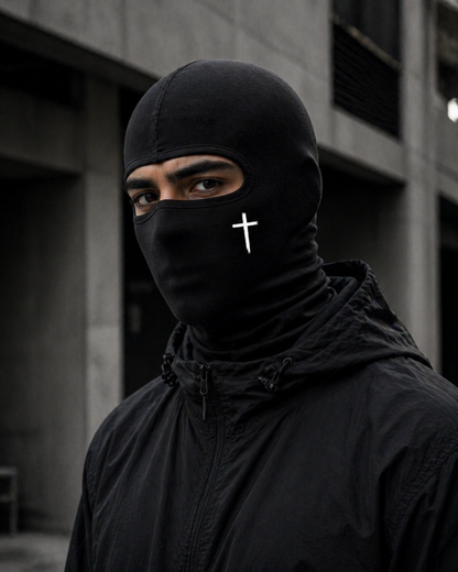 Person wearing a black balaclava with a white cross symbol in an urban setting