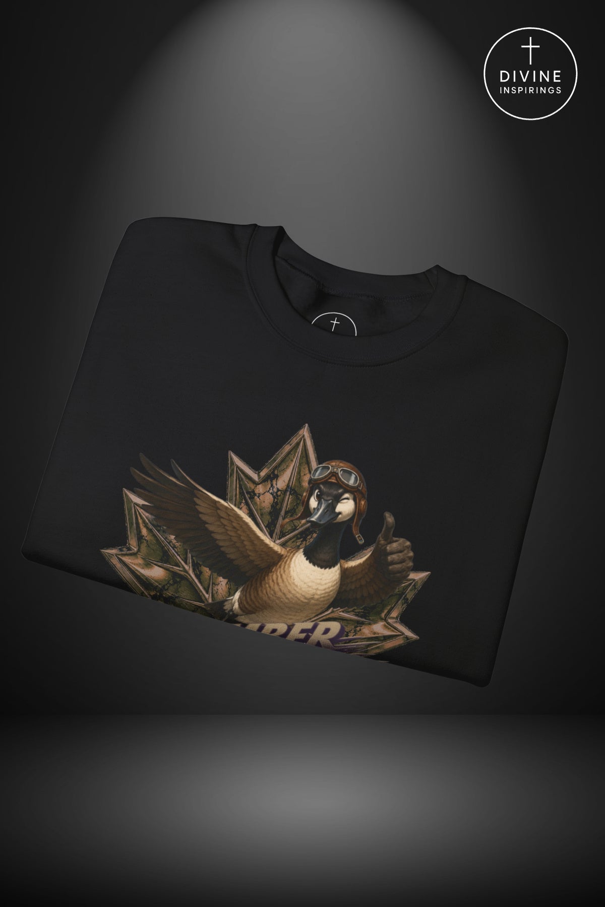 A folded black t-shirt with a graphic of a goose wearing aviator goggles and a helmet, emerging from a fan of dollar bills, displayed on a dark background with a spotlight effect. A 'DIVINE Inspirings' logo is visible in the top right corner.