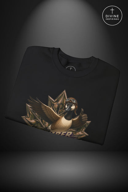 A folded black t-shirt with a graphic of a goose wearing aviator goggles and a helmet, emerging from a fan of dollar bills, displayed on a dark background with a spotlight effect. A 'DIVINE Inspirings' logo is visible in the top right corner.