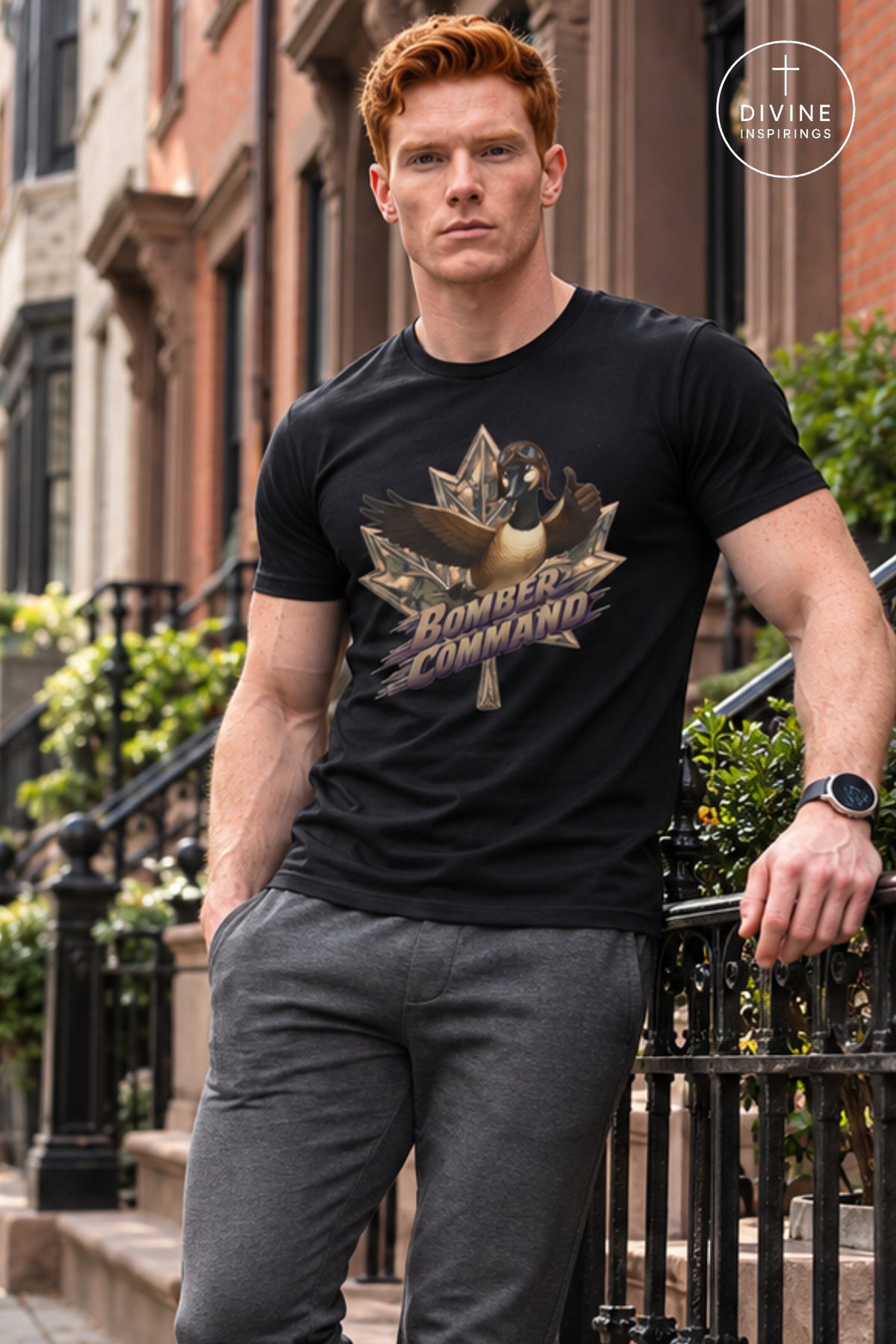 A man with red hair wearing a black graphic t-shirt and gray pants, leaning against a black metal railing on outdoor city steps. The t-shirt features a metallic gold and bronze bomber jacket graphic with a dog inside a maple leaf and the text 'BOMBER COMMAND'.