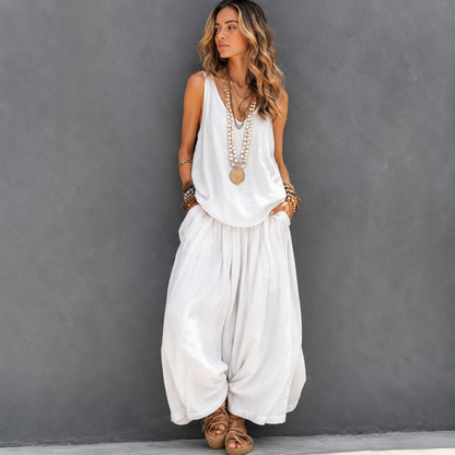Woman wearing a white sleeveless top and harem pants against a gray background