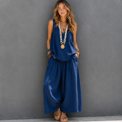 Woman wearing a blue sleeveless top and wide-leg pants against a gray wall.