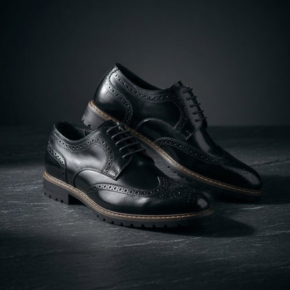 Pair of black leather dress shoes on a dark surface with a dark background