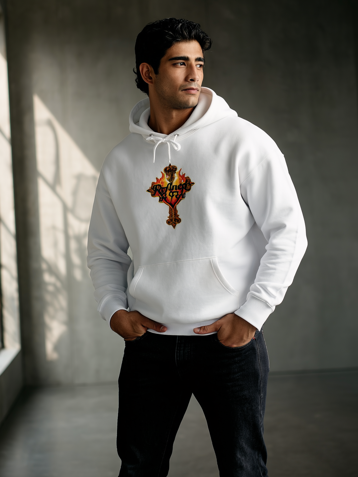 Man wearing a white hoodie with a logo in a room with a window casting shadows.