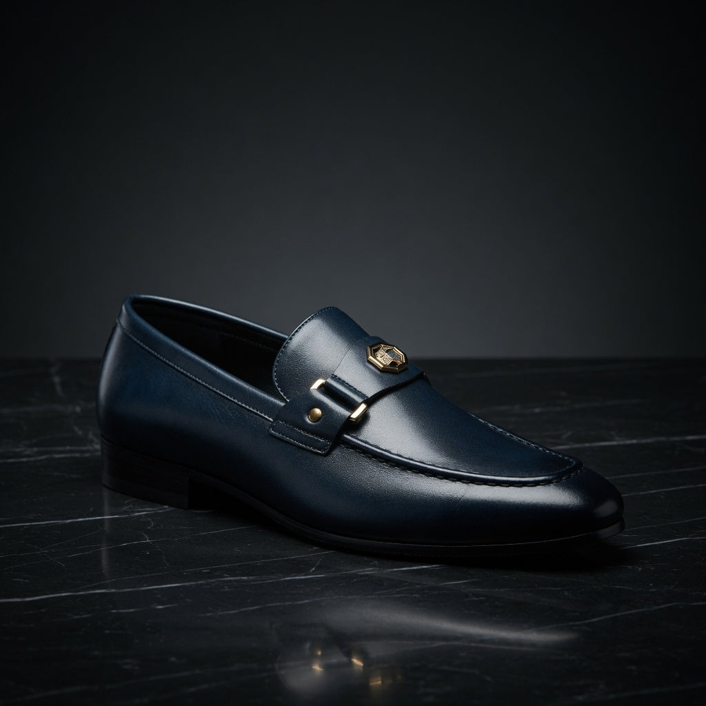 Black loafer shoe with a gold buckle on a dark surface