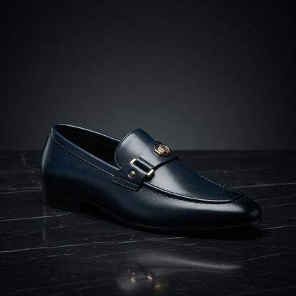 Black loafer shoe with a gold buckle on a dark surface