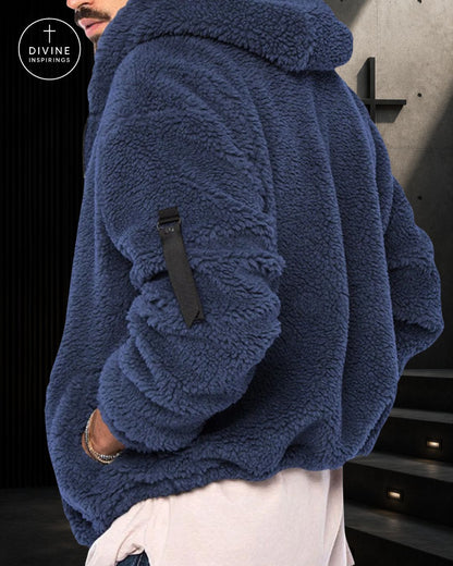 A close-up of a person wearing a plush navy blue sherpa fleece hoodie with a black strap detail on the sleeve, paired with light-colored pants. The DIVINE INSPIRINGS logo is visible in the top-left corner.