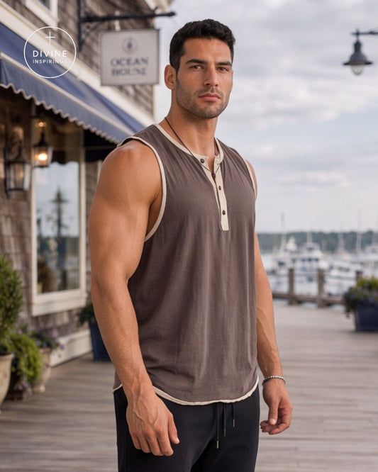 A muscular man wearing a brown sleeveless henley tank top with beige trim, standing on a wooden boardwalk next to a waterfront with boats in the background. A Divine Image logo is visible in the top left corner.