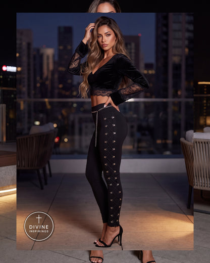 A woman models a black velvet long-sleeve crop top and matching black lace-paneled leggings with side cutouts and silver rhinestone trim, standing on a rooftop terrace at night with a city skyline in the background. A Divine Inspirings logo is visible in the lower left.