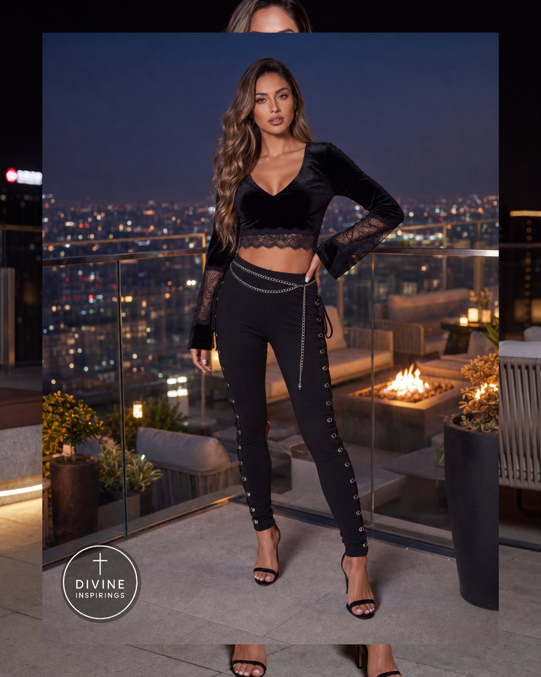 A woman models a black velvet and lace two-piece outfit consisting of a long-sleeve crop top and matching high-waisted skinny pants with side lace-up details, standing on a rooftop terrace at night with a city skyline background.