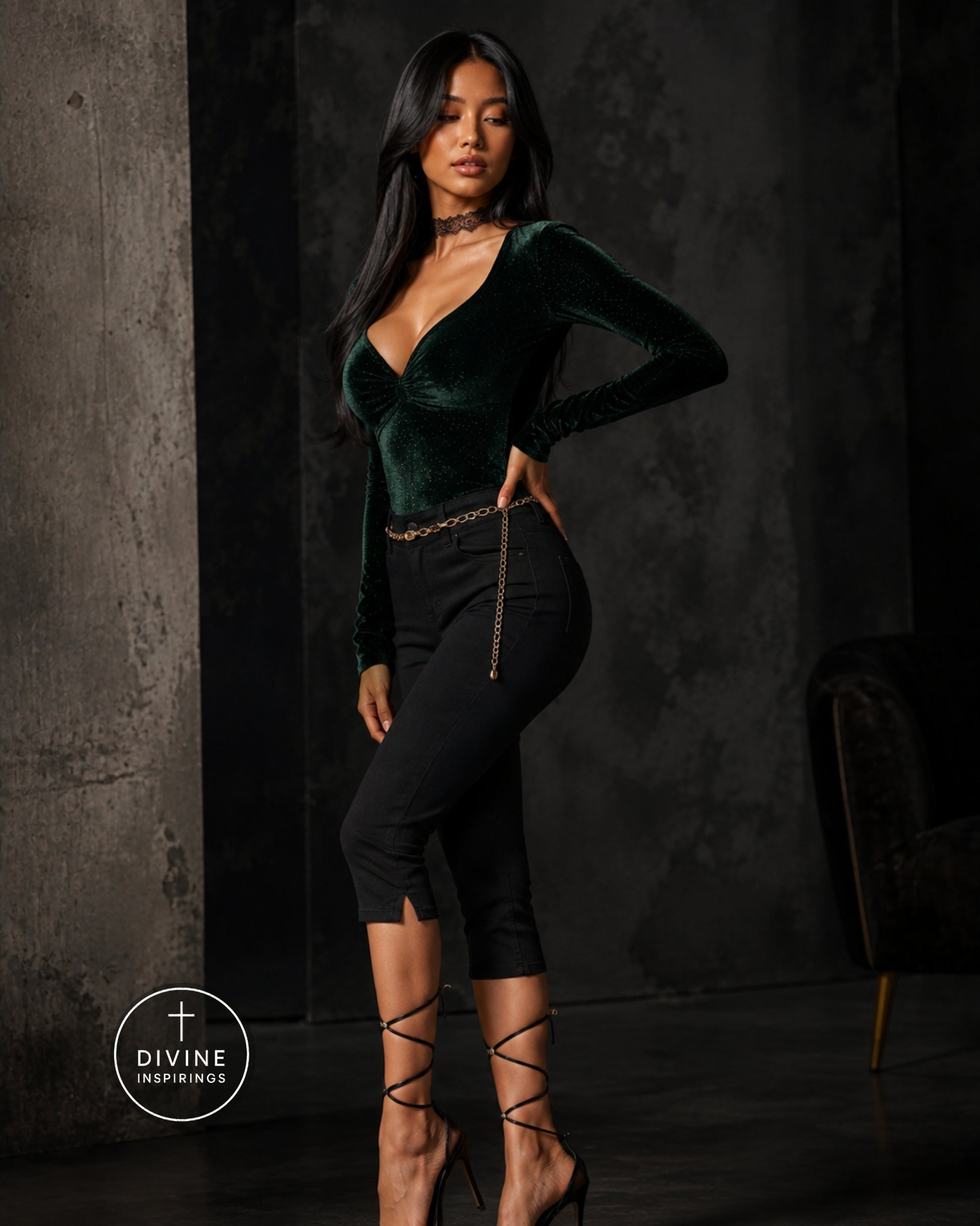 A woman models a dark green velvet long-sleeve top paired with black capri pants featuring a gold chain detail at the waist, set against a dark textured studio background.