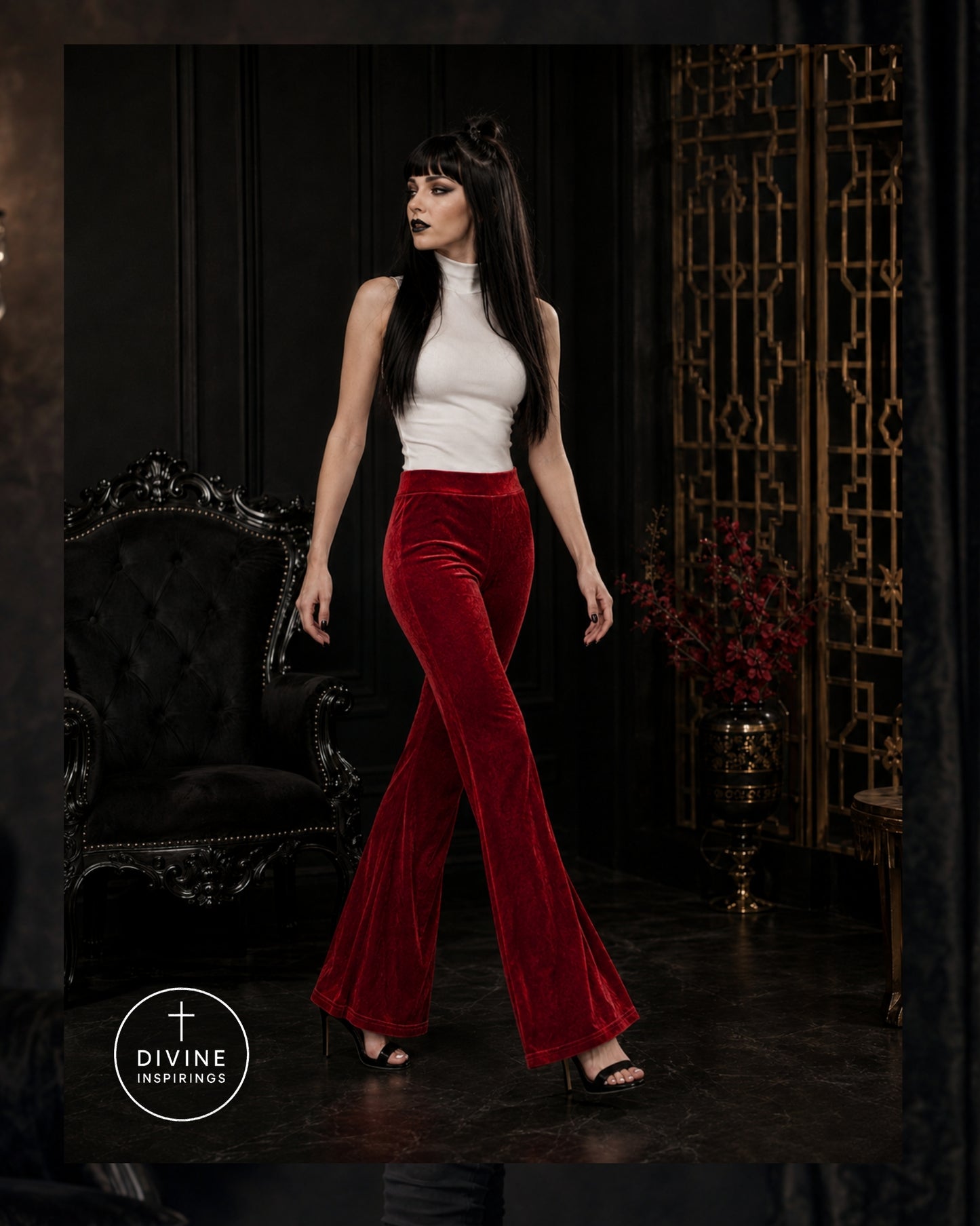 A woman models a two-piece outfit consisting of a white sleeveless mock-neck top and high-waisted, red velvet flare pants. She is standing in a dark, elegant room with a black velvet armchair and a gold decorative screen behind her.