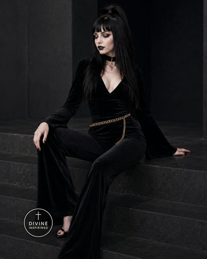 A model with long black hair and dark makeup sits on dark stone steps wearing a black velvet long-sleeve outfit with a gold chain belt detail. A circular 'DIVINE INSPIRINGS' logo is visible in the bottom-left corner.