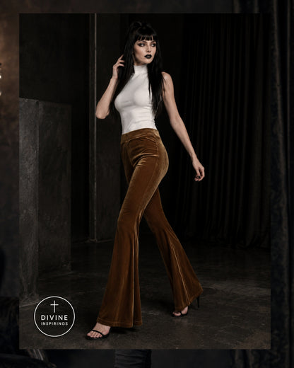 A model wearing a white mock-neck top and brown velvet flare pants walks in a dark studio setting. A circular logo for 'DIVINE INSPIRINGS' is visible in the bottom-left corner.
