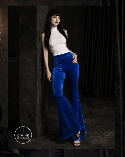 A model wearing a white mock-neck top and vibrant royal blue velvet flared pants, posing in a dark, moody studio setting with a visible 'DIVINE INSPIRINGS' logo in the bottom-left corner.
