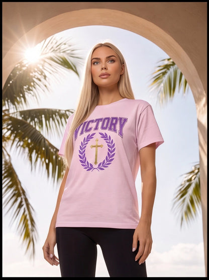 Woman wearing a pink t-shirt with 'VICTORY' and a cross design, standing in front of palm trees.