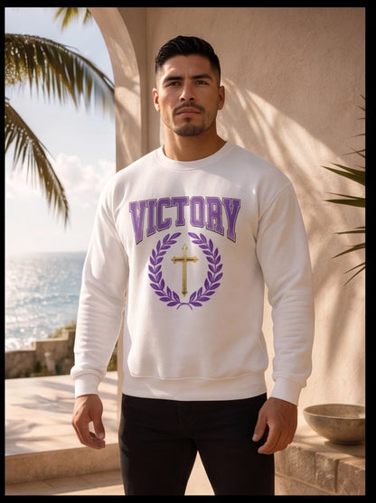 Man wearing a white sweatshirt with 'VICTORY' and a cross design, standing outdoors with palm trees and ocean in the background.