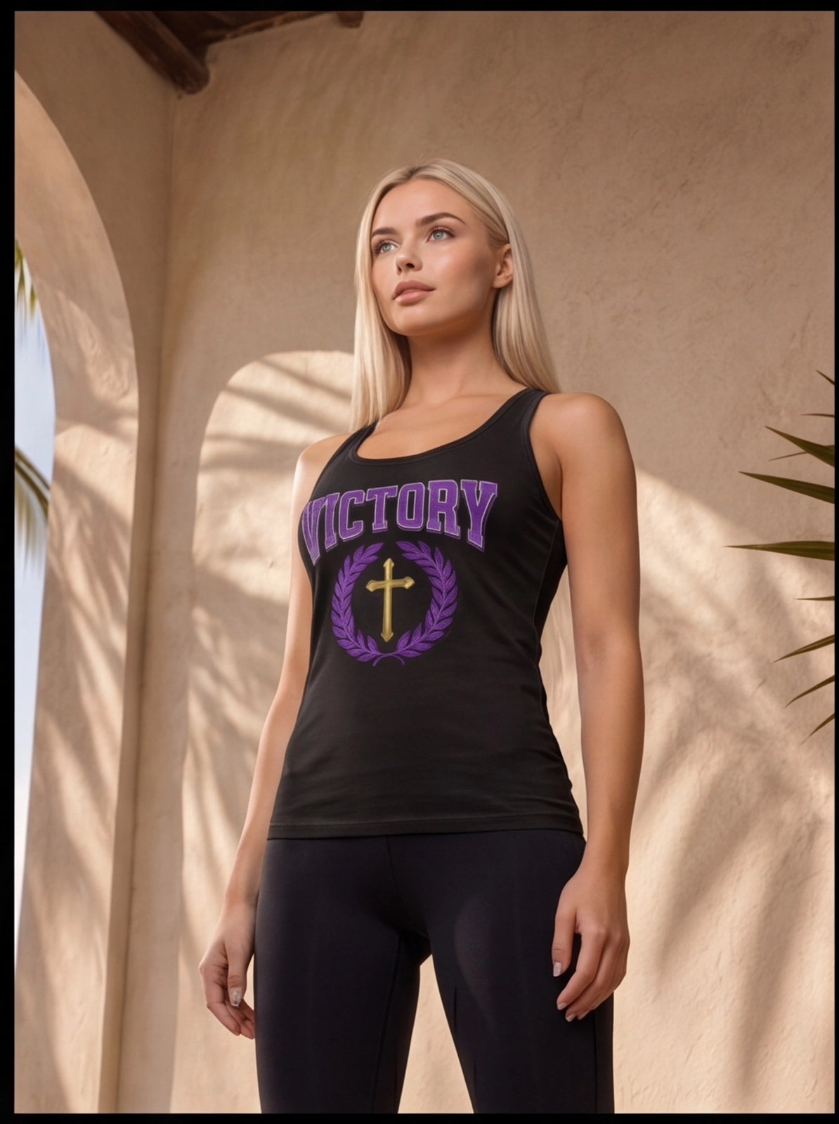 Woman wearing a black tank top with 'VICTORY' and a cross design, standing against a beige wall.