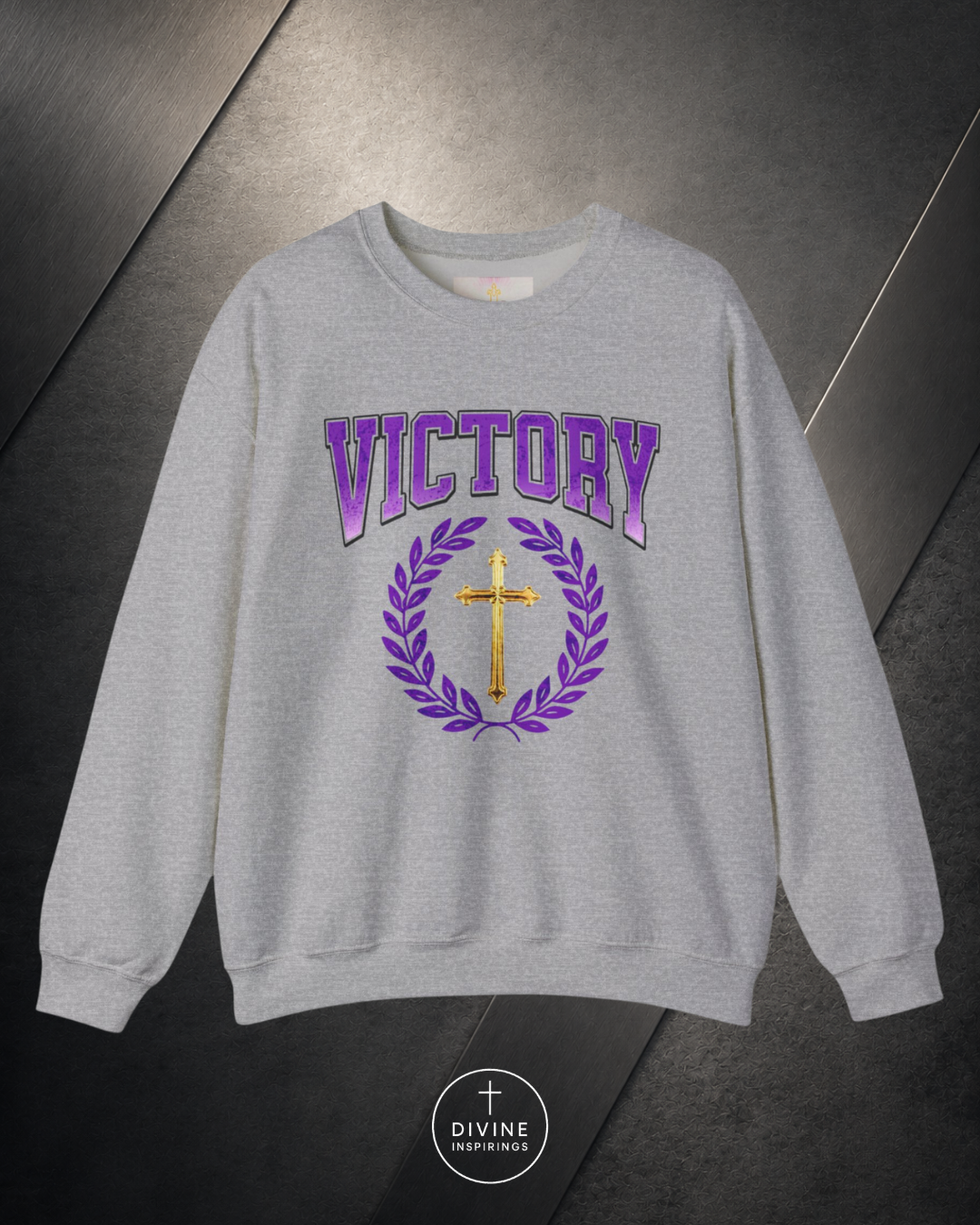 Gray sweatshirt with 'VICTORY' and cross design on a metallic surface, featuring the brand 'Divine Emporium'.