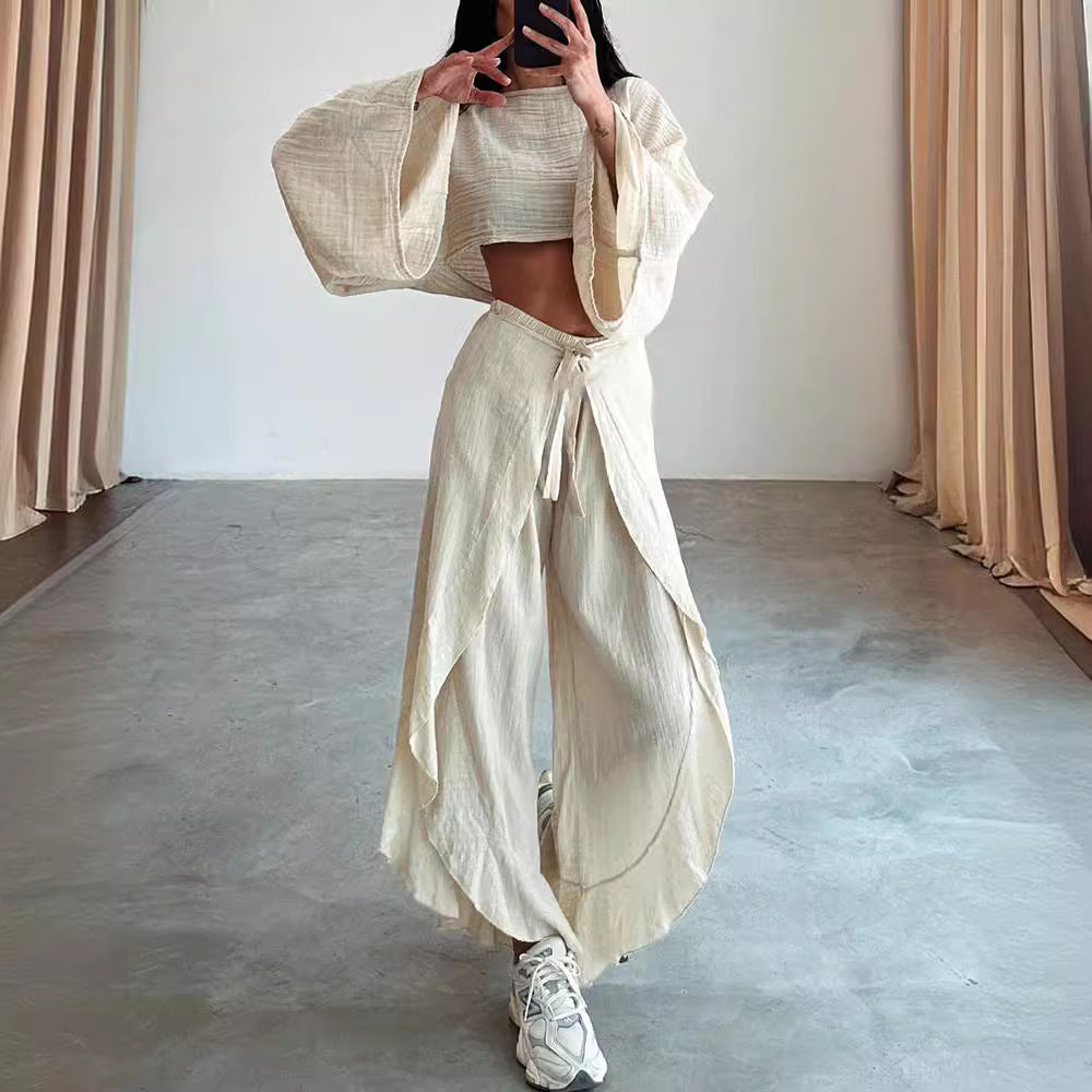 Person wearing a beige outfit with wide-legged pants and a top, standing in a minimalistic room with beige curtains.